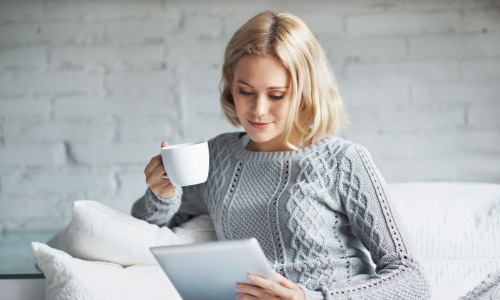 a woman holding a coffee cup looking at a tablet